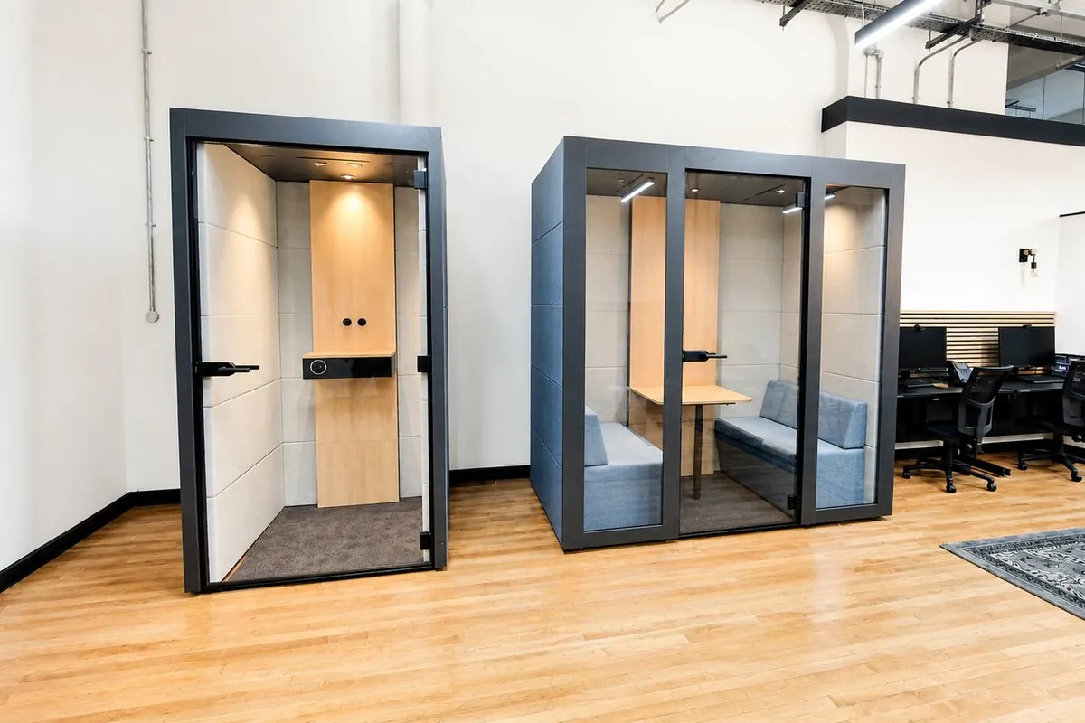 A single phone booth and a two-seat glazed meeting pod on an oak floor in an open-plan office